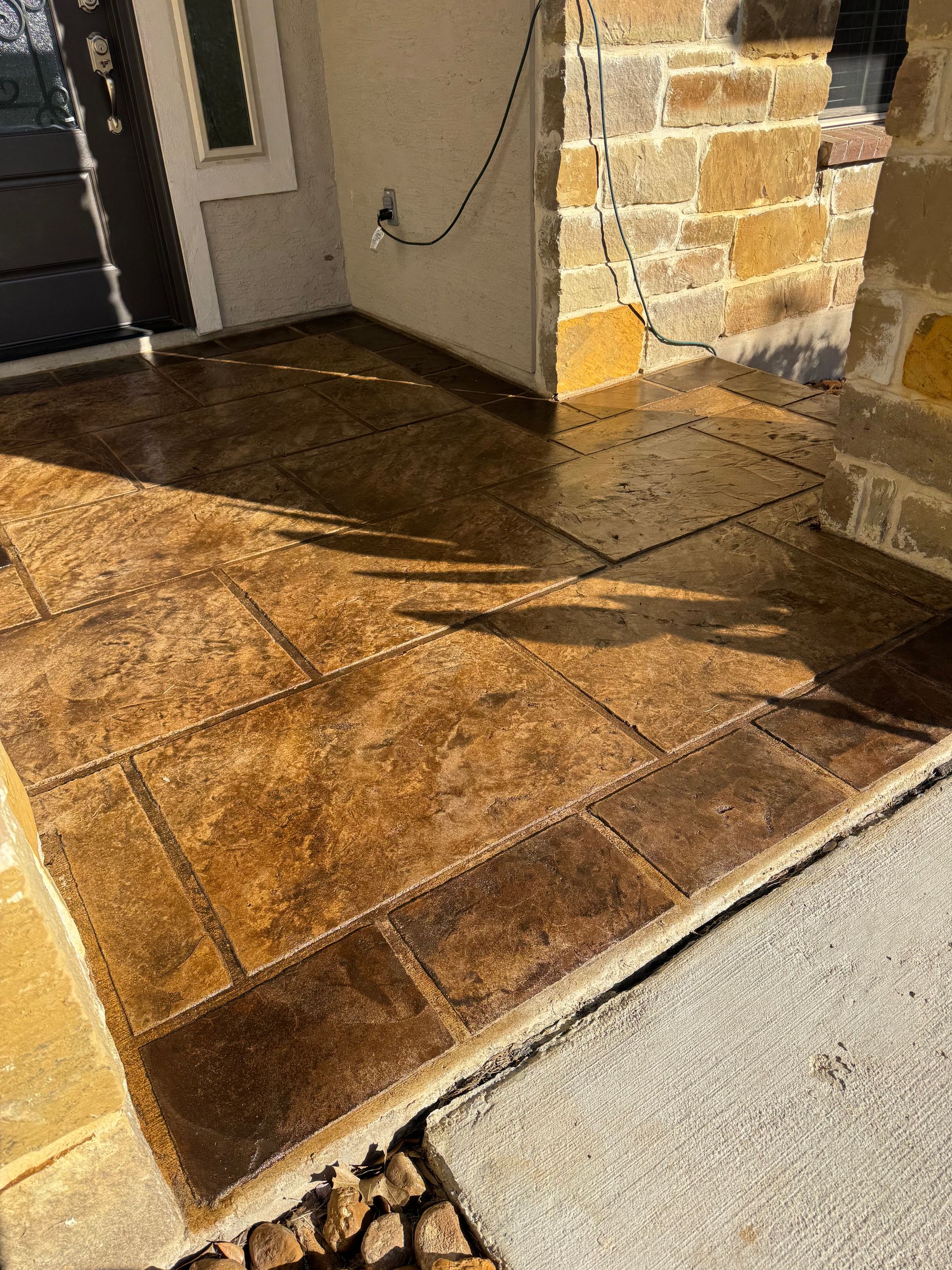 Stone porch with wet tan tiles and a house doorway beside a sunlit walkway