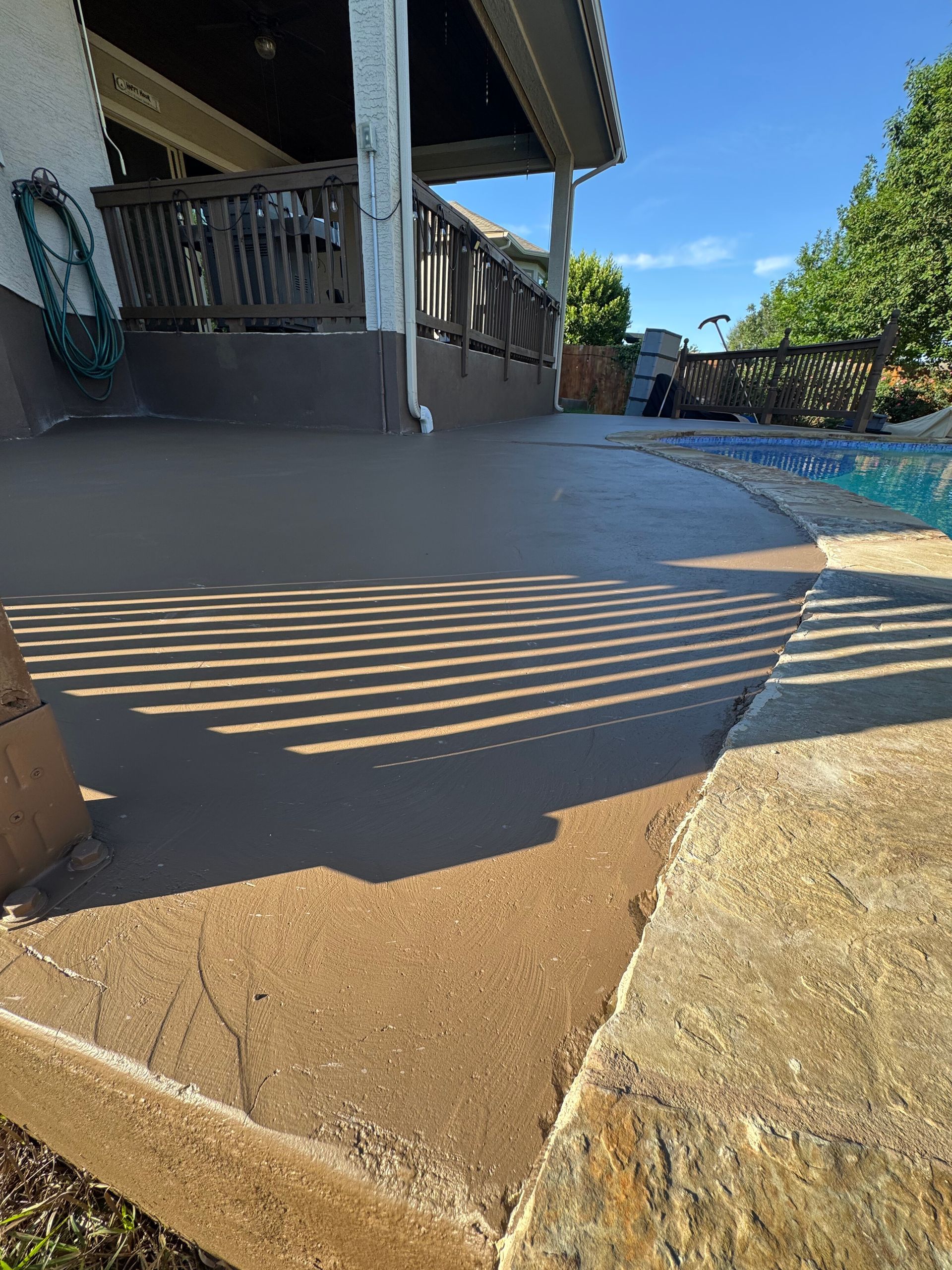 Patio with striped sunlight shadows, stone steps, and a pool beside a house porch