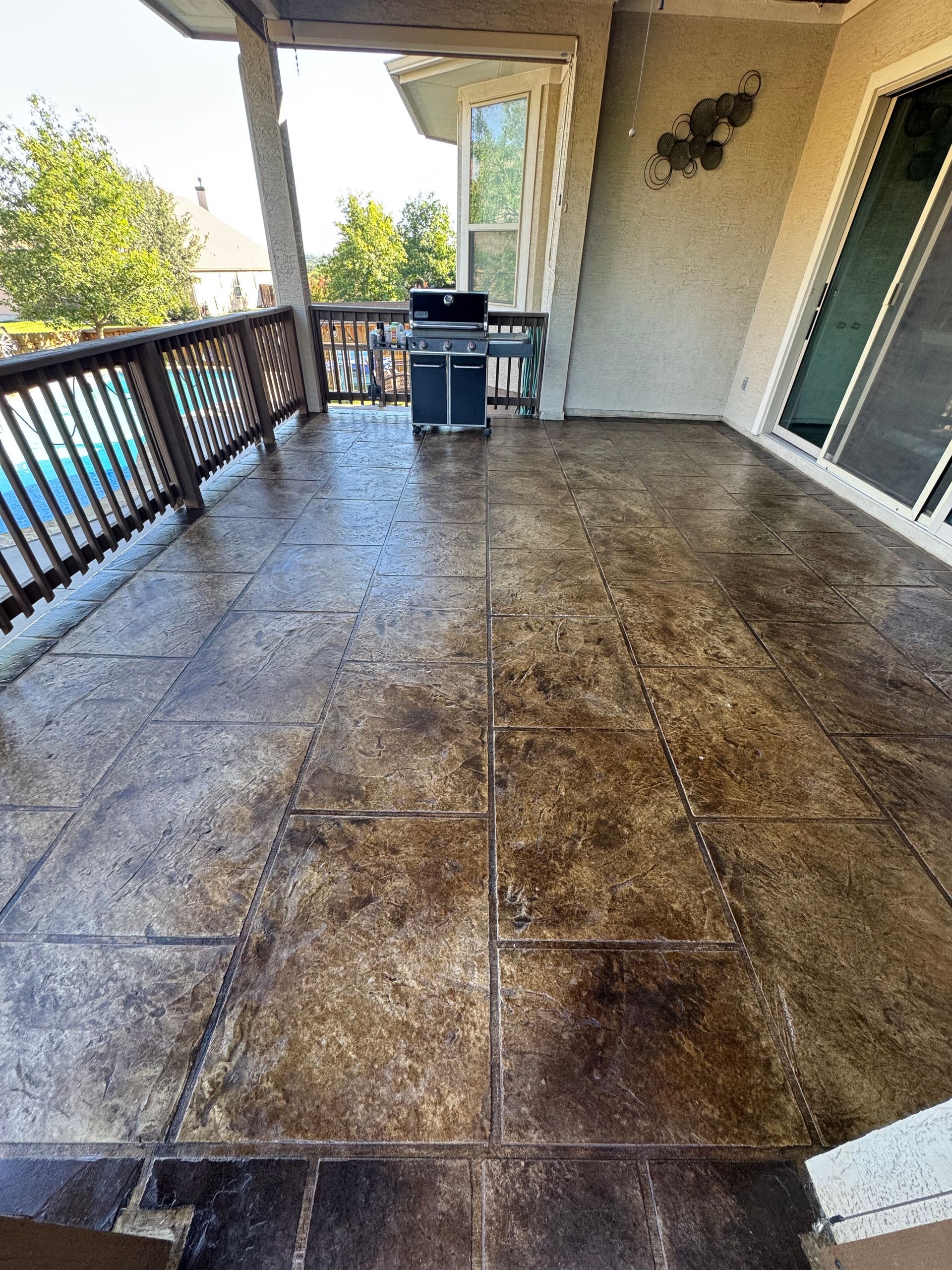 Covered patio with stamped concrete floor, railing, sliding door, and outdoor table and chairs.