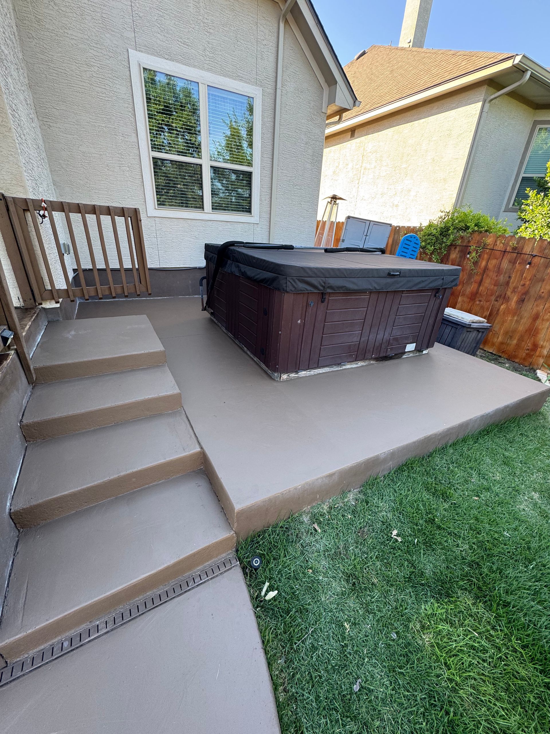 Backyard patio with steps, a hot tub, and a grassy lawn beside a house