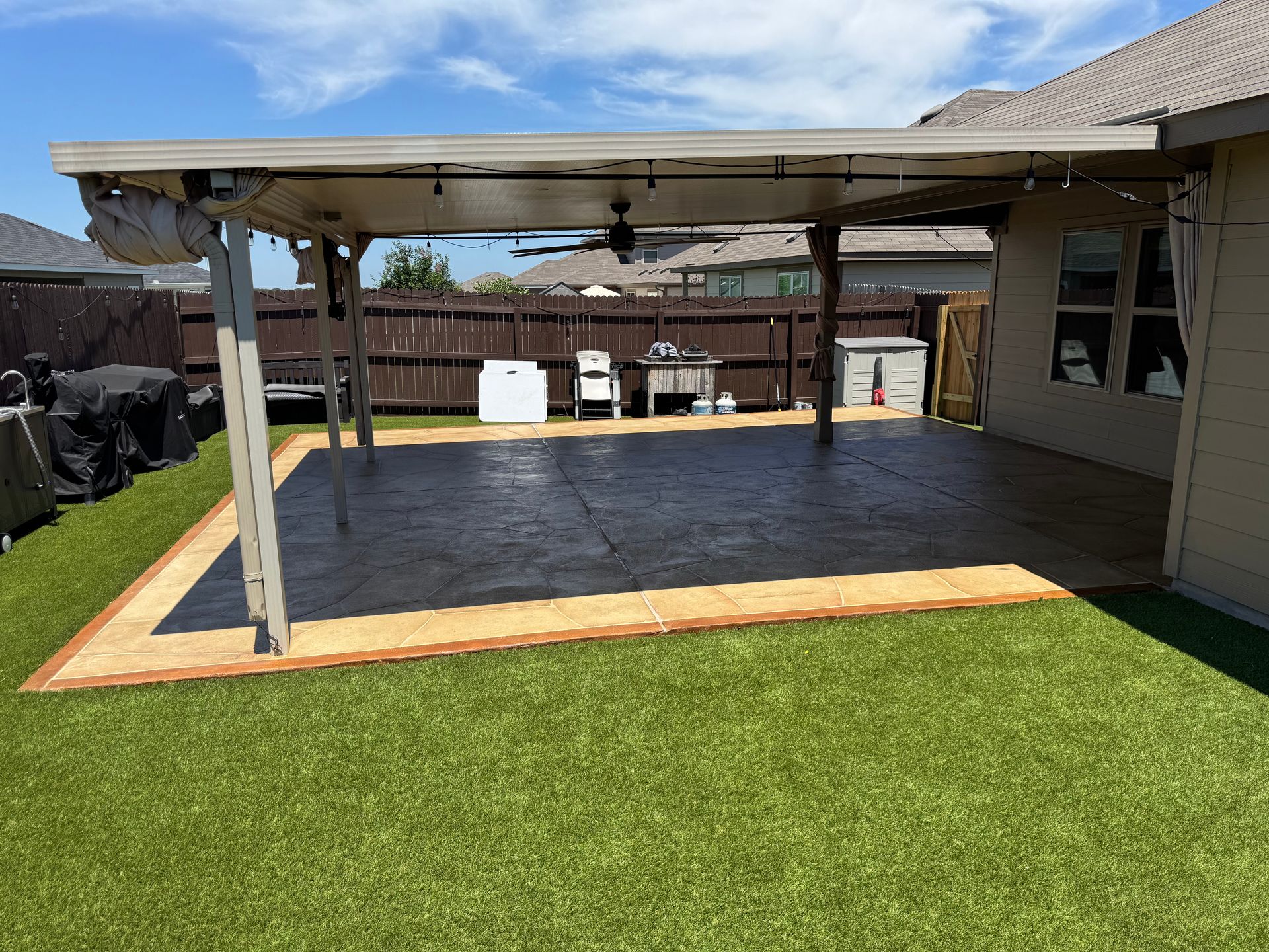 Covered patio with concrete floor, wooden posts, and green lawn in a backyard