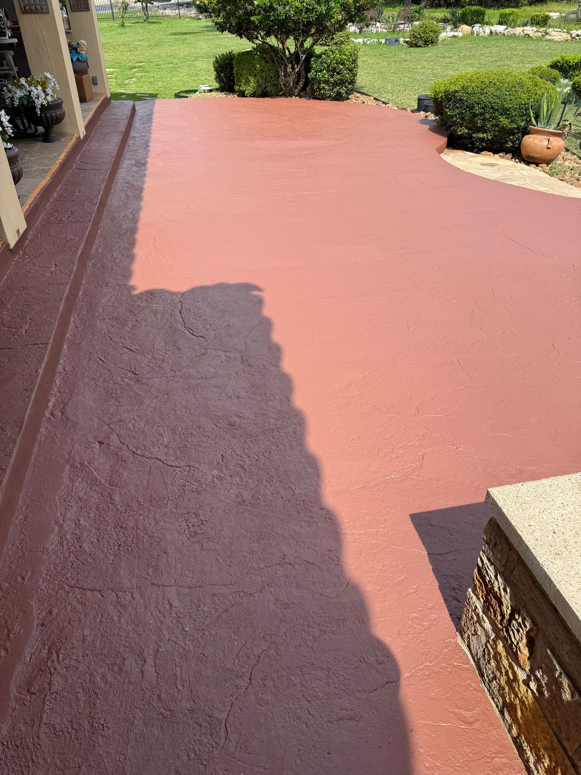 Red-coated walkway beside a house, with garden plants and sunlight shadows.