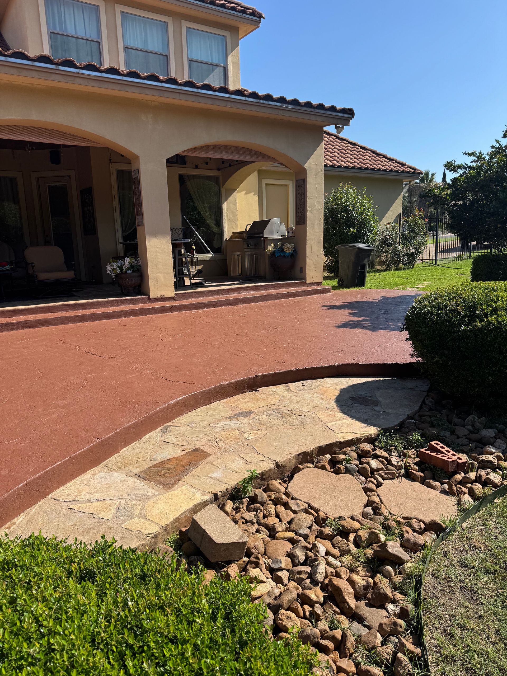 Sunny house entrance with arched porch, red driveway, and landscaped garden path