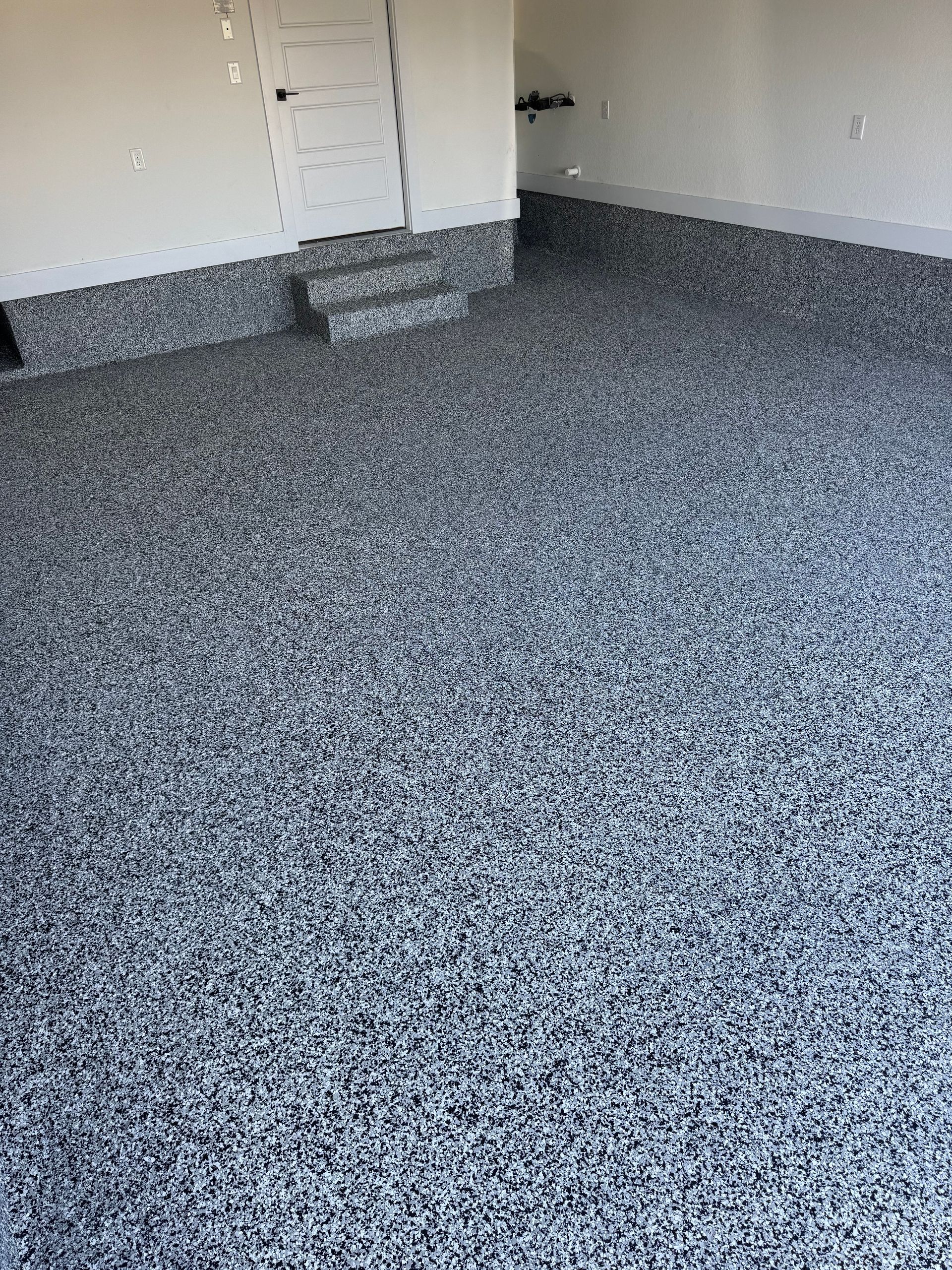 Empty room with gray speckled carpet and white walls, plus a small step or platform in the corner