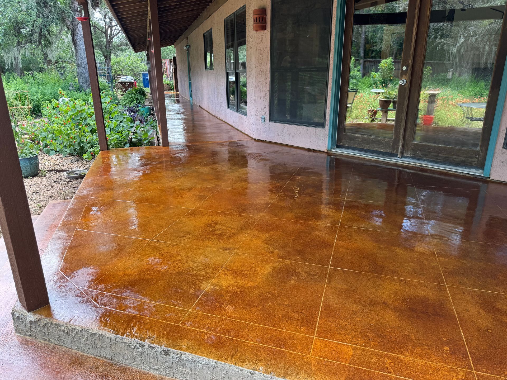 Rainy porch with glossy orange floor, white wall, glass doors, and garden view outside