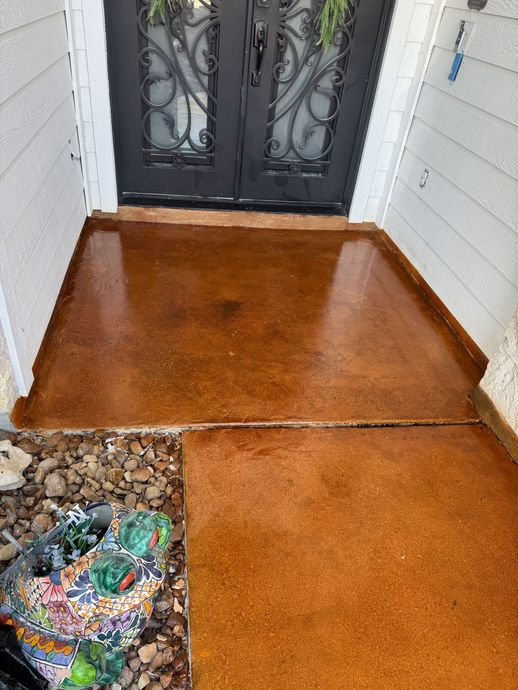Rust-colored front porch with black double doors and a small rock bed at the lower left.