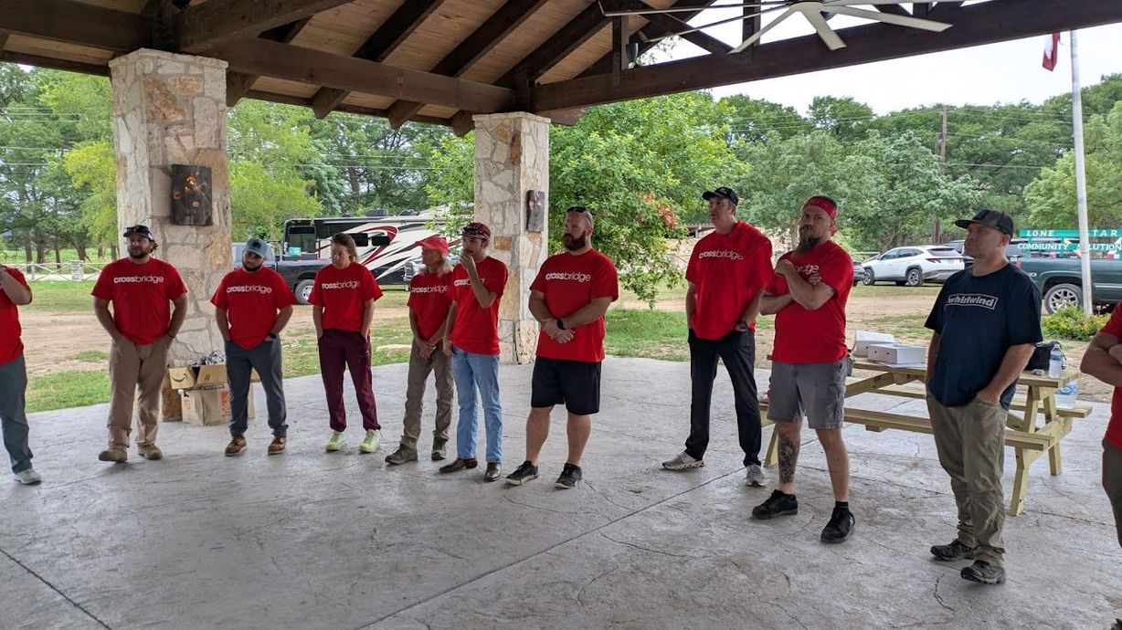 Group of people in red shirts standing under a pavilion, facing the camera.