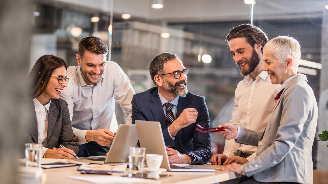 Colleagues smiling and discussing documents around a table in a bright office meeting room