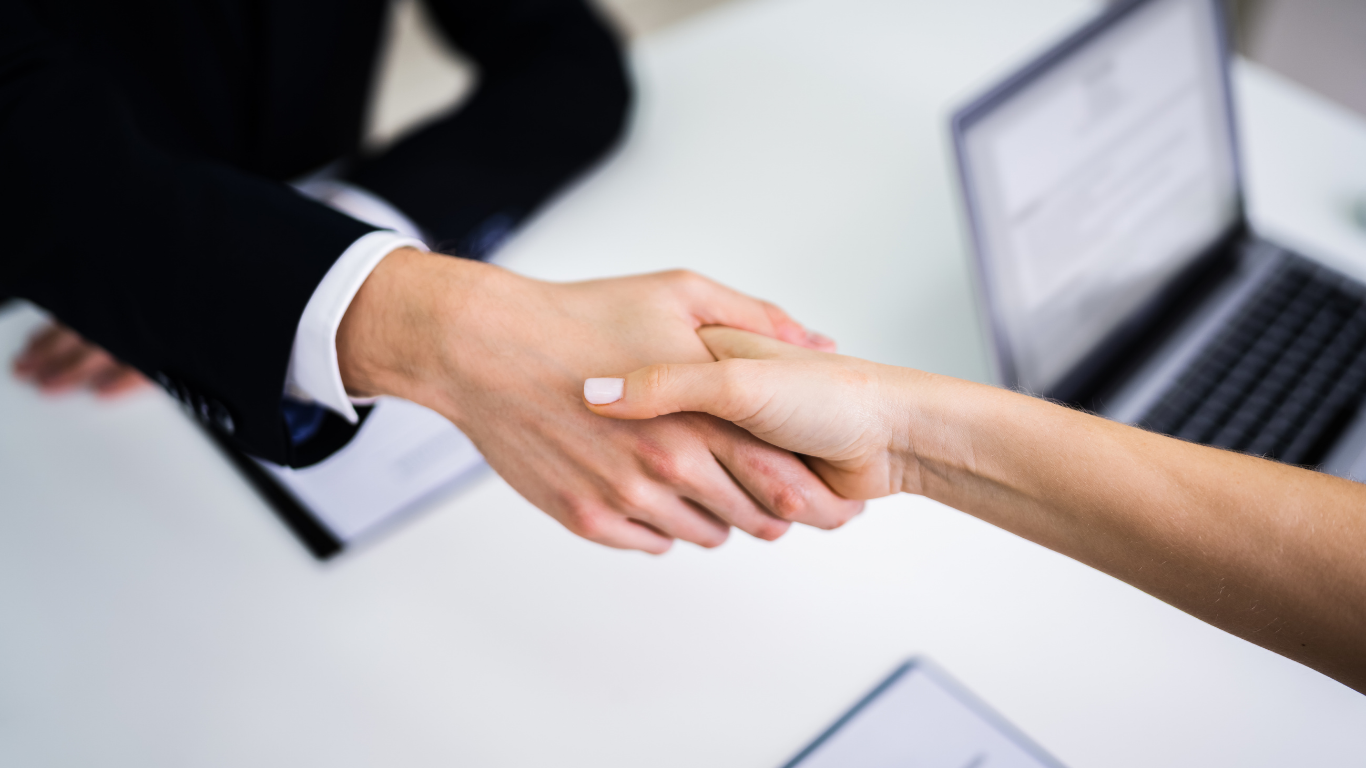Business handshake over a desk with a laptop in the background