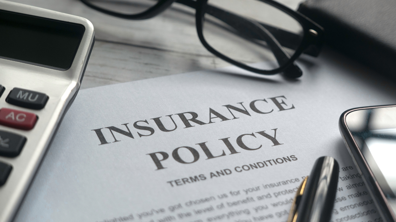 Insurance policy document on a desk with a calculator, phone, and pen.