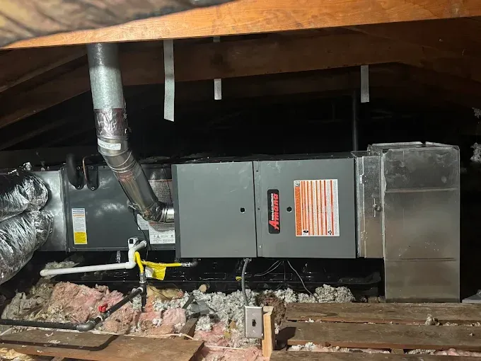 HVAC unit in attic, with ductwork and insulation. Gray metal equipment, under wooden beams.