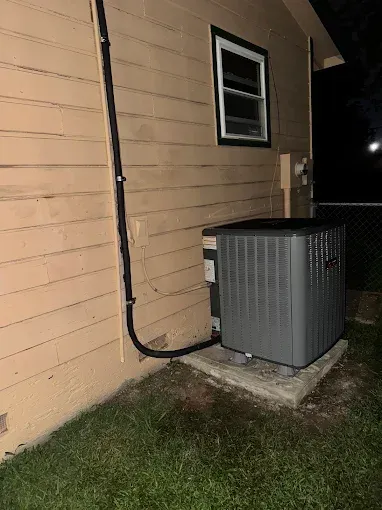 Air conditioner unit outside a beige building, near a window at night.