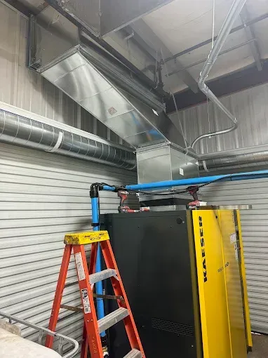 Air compressor unit with ventilation ductwork and a red ladder in an industrial setting.