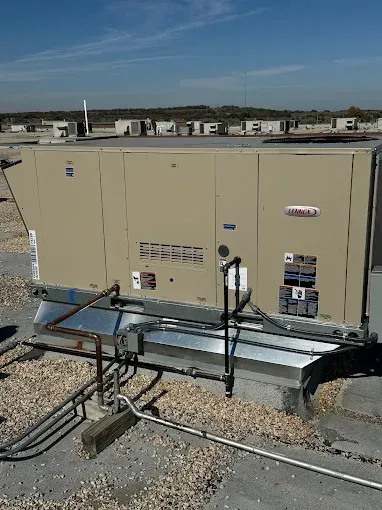 Rooftop HVAC unit, beige, with pipes, surrounded by gravel, under a blue sky.
