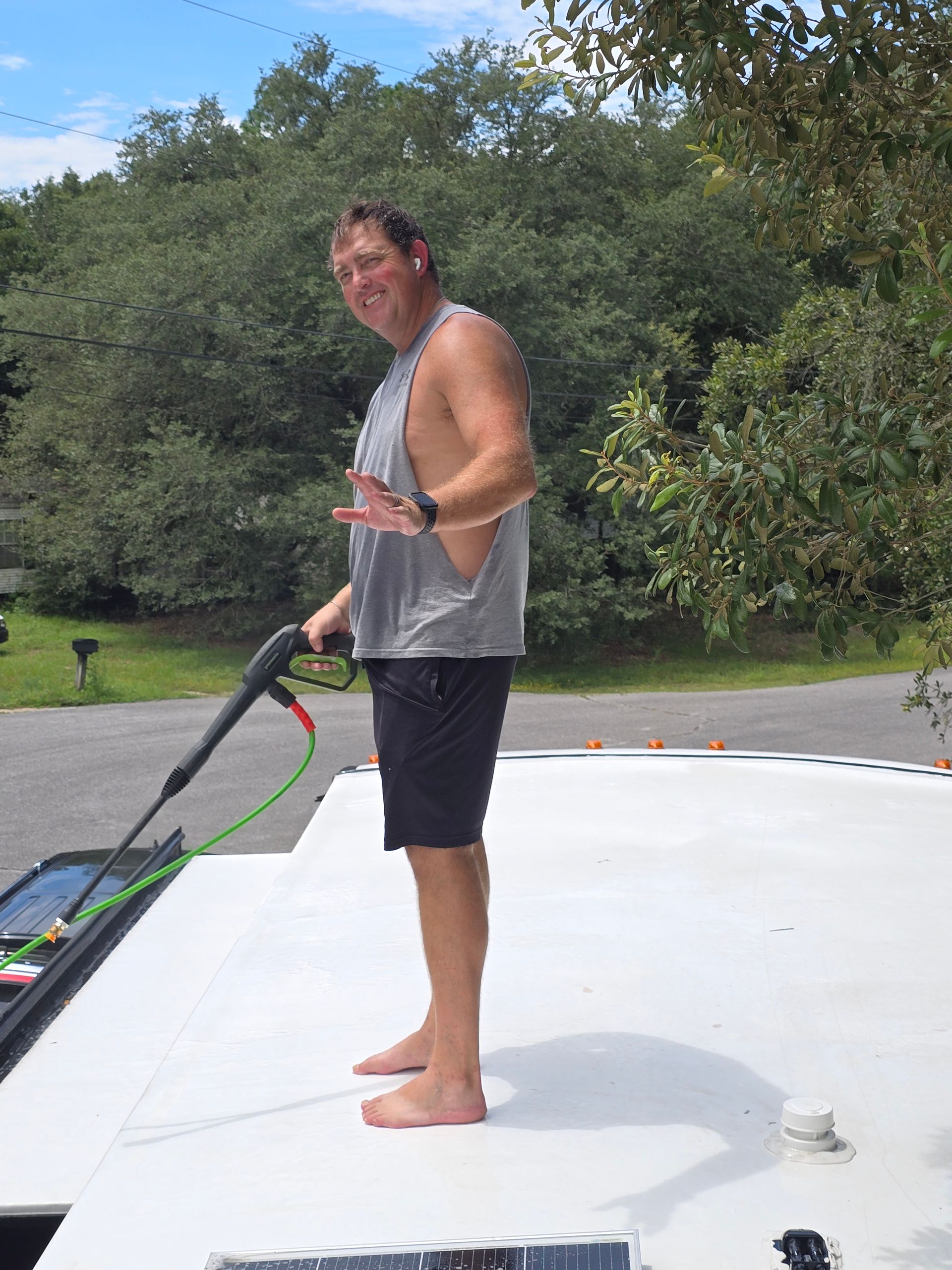 Person standing on a white boat deck holding a long pole, with trees and water in the background