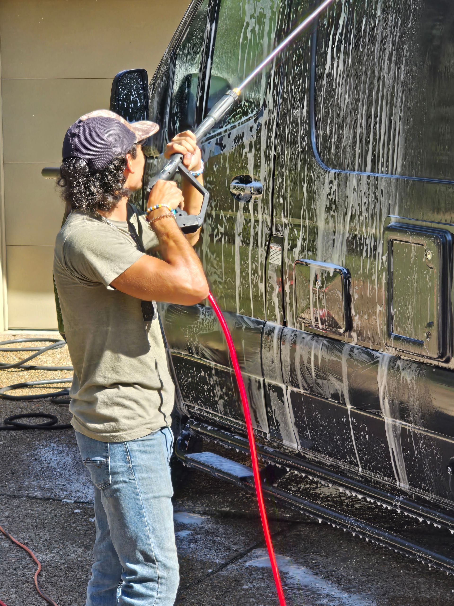 Person using a green hose on a white rooftop, standing near a square roof vent.