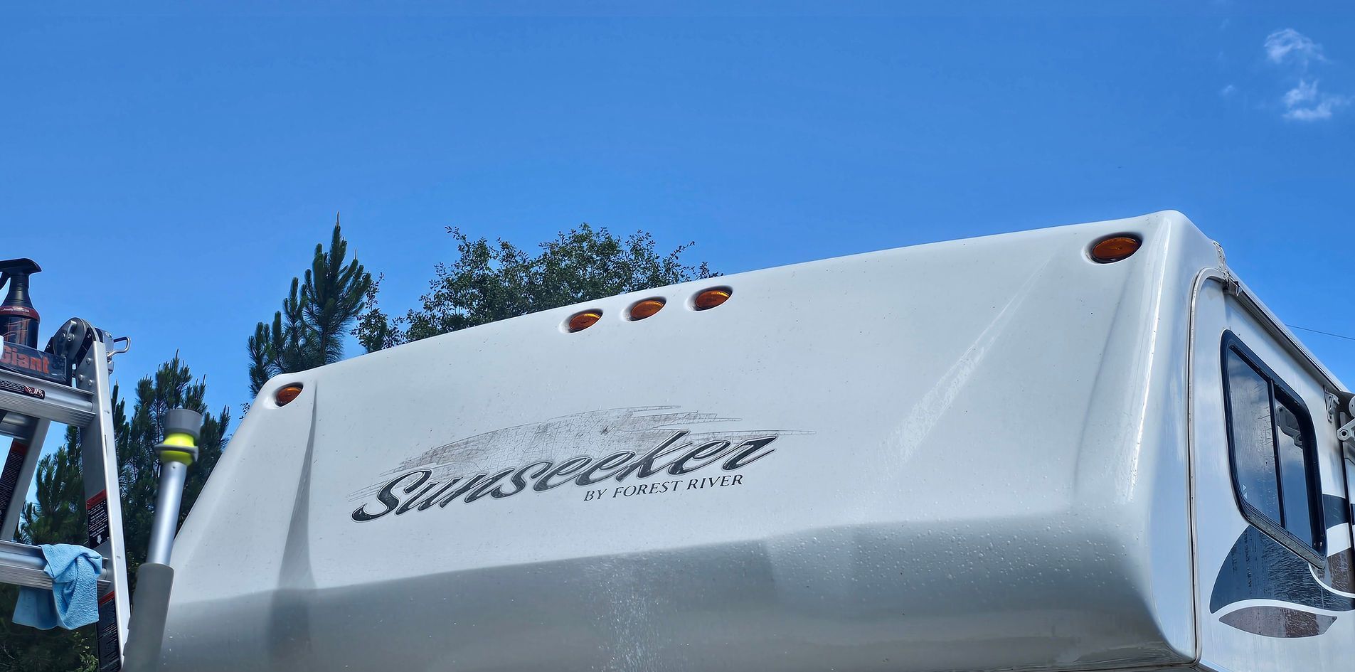 White RV trailer with a logo parked outdoors under a blue sky.