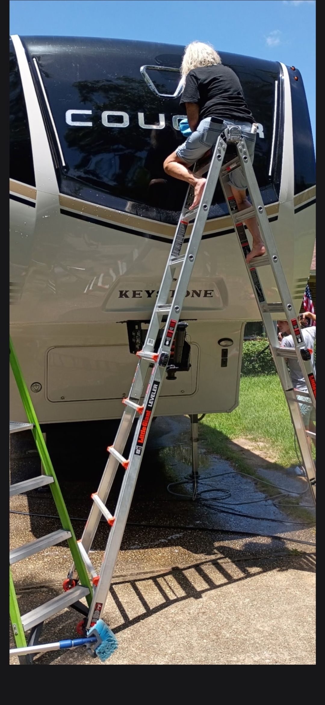 Person on a ladder painting a boat’s hull beside a blue tarp-covered area outdoors