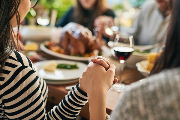 a group of people are sitting at a table holding hands and praying .