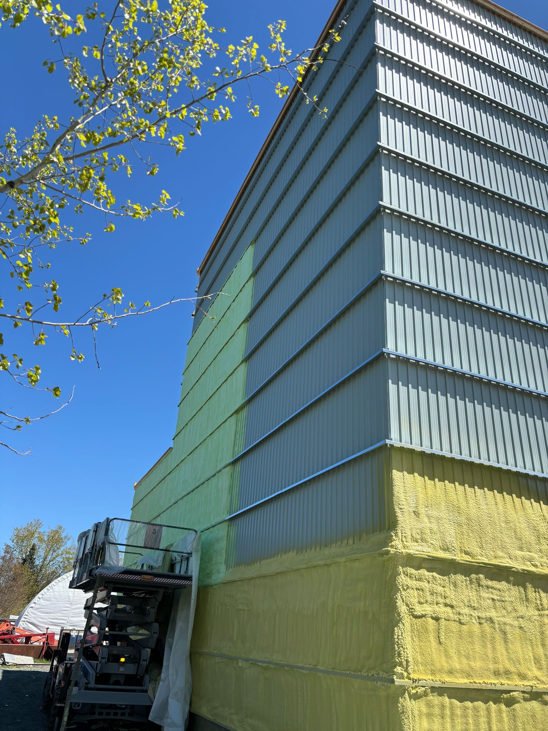 Construction d'un extérieur de bâtiment avec un bardage en tôle ondulée argentée, une isolation jaune