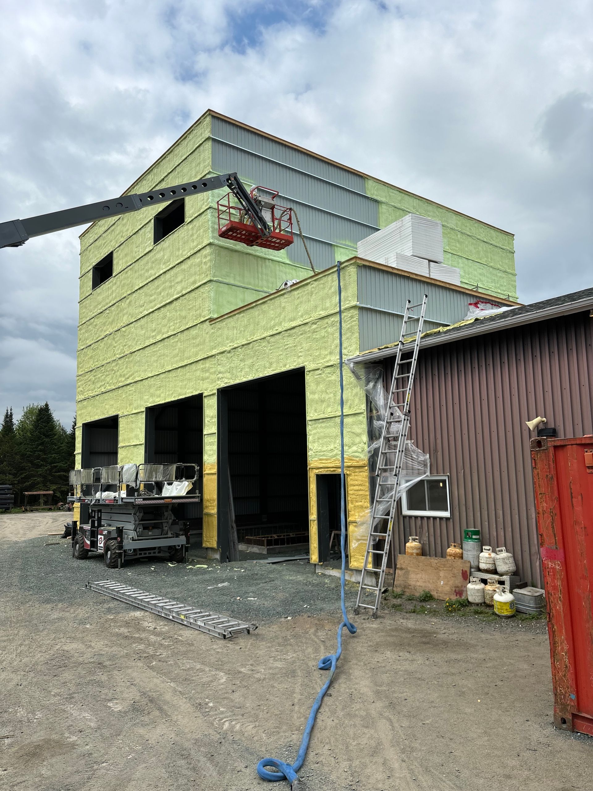 Chantier de construction avec un ascenseur en fonctionnement à proximité d'un bâtiment, qui dispose d'une isolation verte