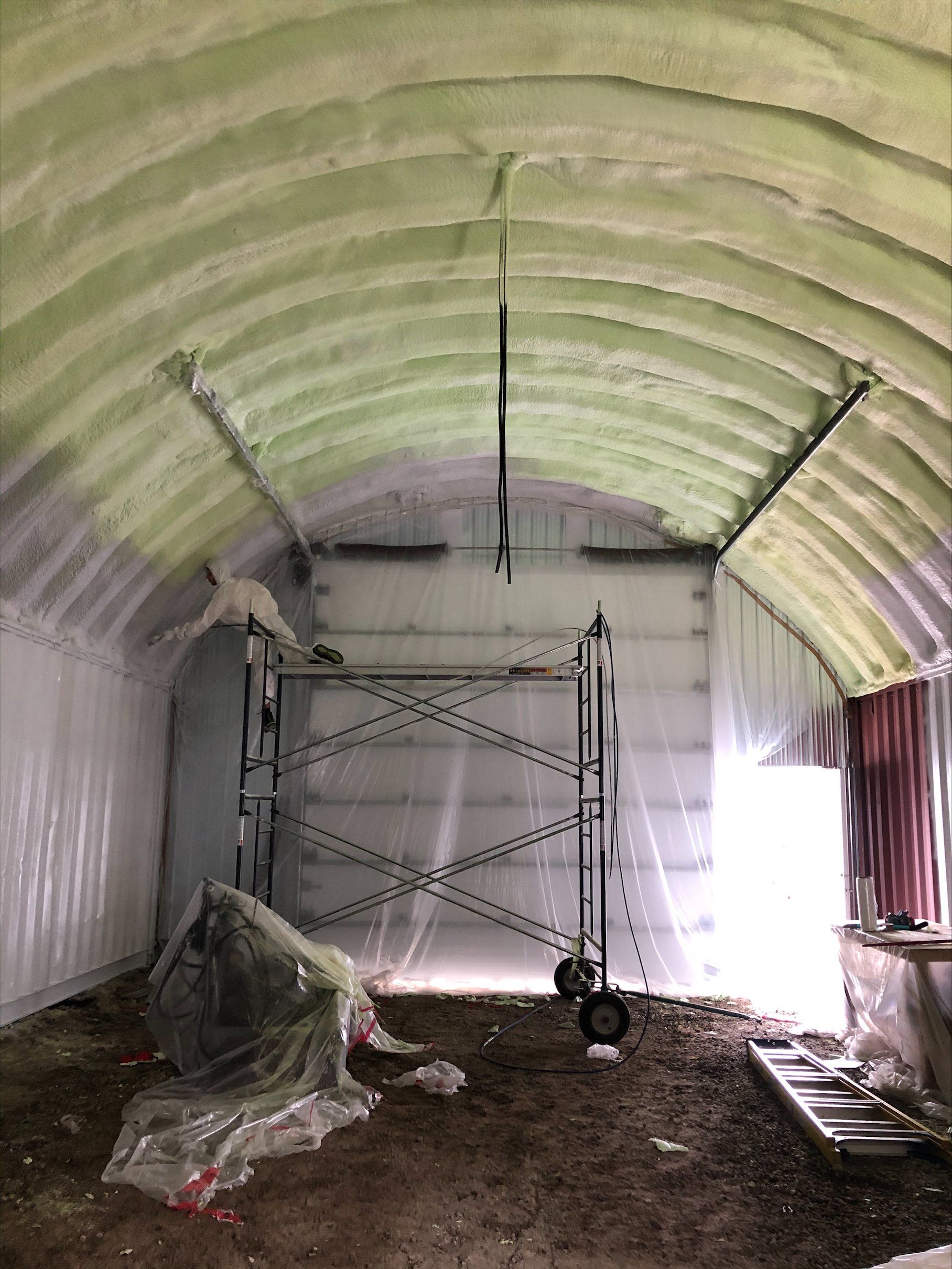 Vue intérieure d'un bâtiment à toit incurvé avec isolation en mousse projetée. Un ouvrier du bâtiment est présent