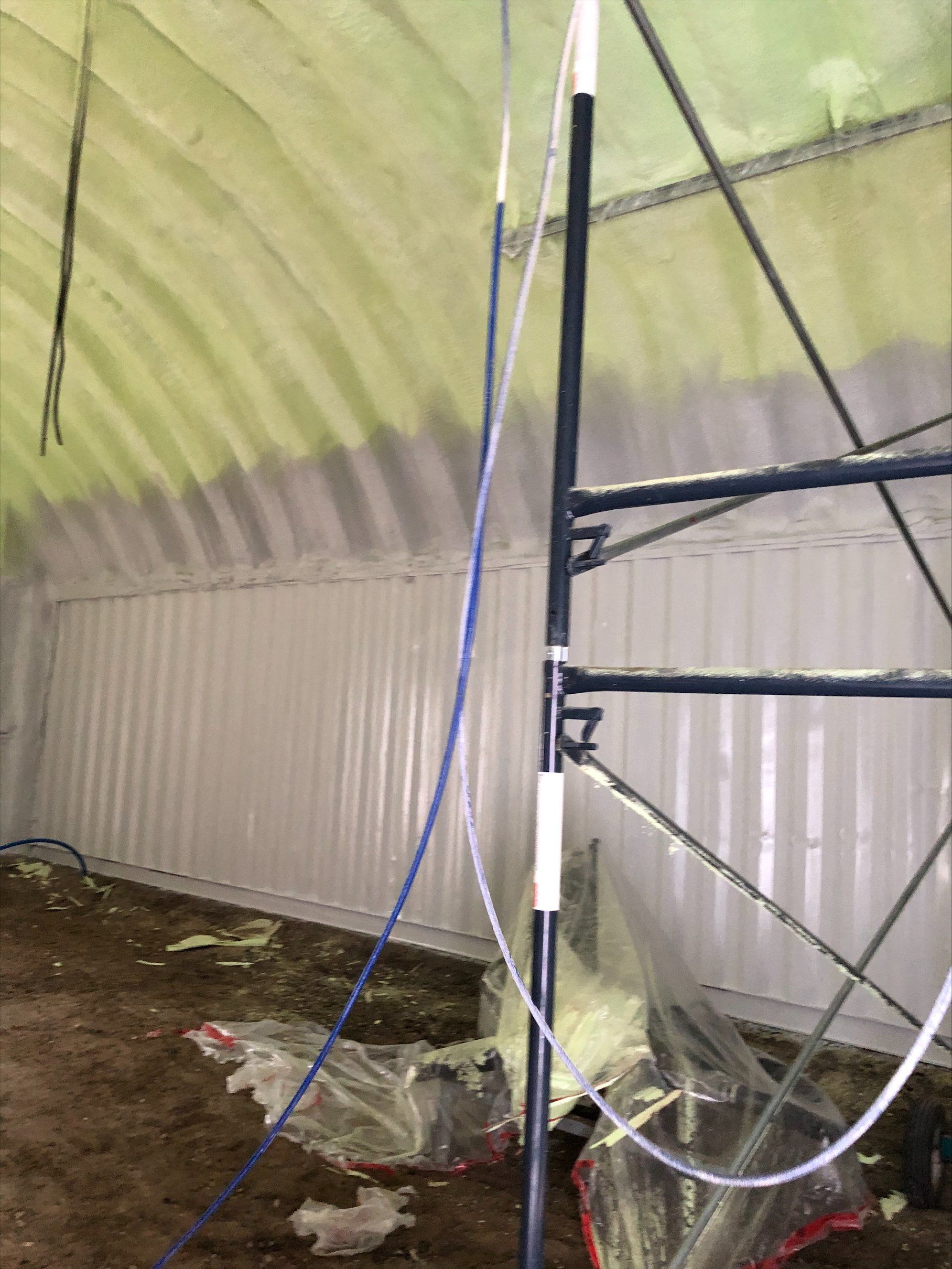 Intérieur d'une structure aux murs blancs avec isolation en mousse projetée verte sur le plafond voûté.