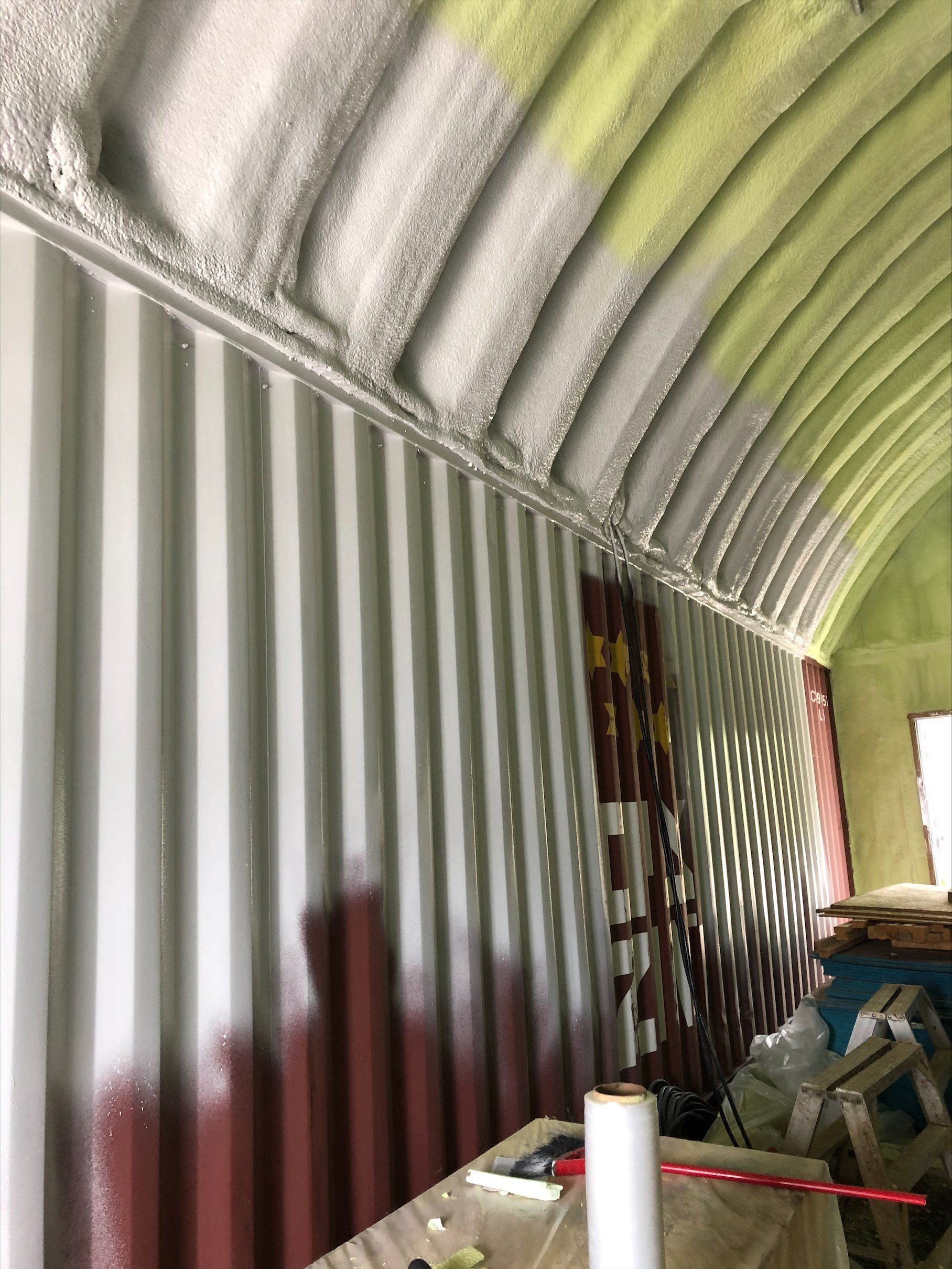 Intérieur d'une structure métallique ondulée avec isolation en mousse pulvérisée sur le plafond incurvé