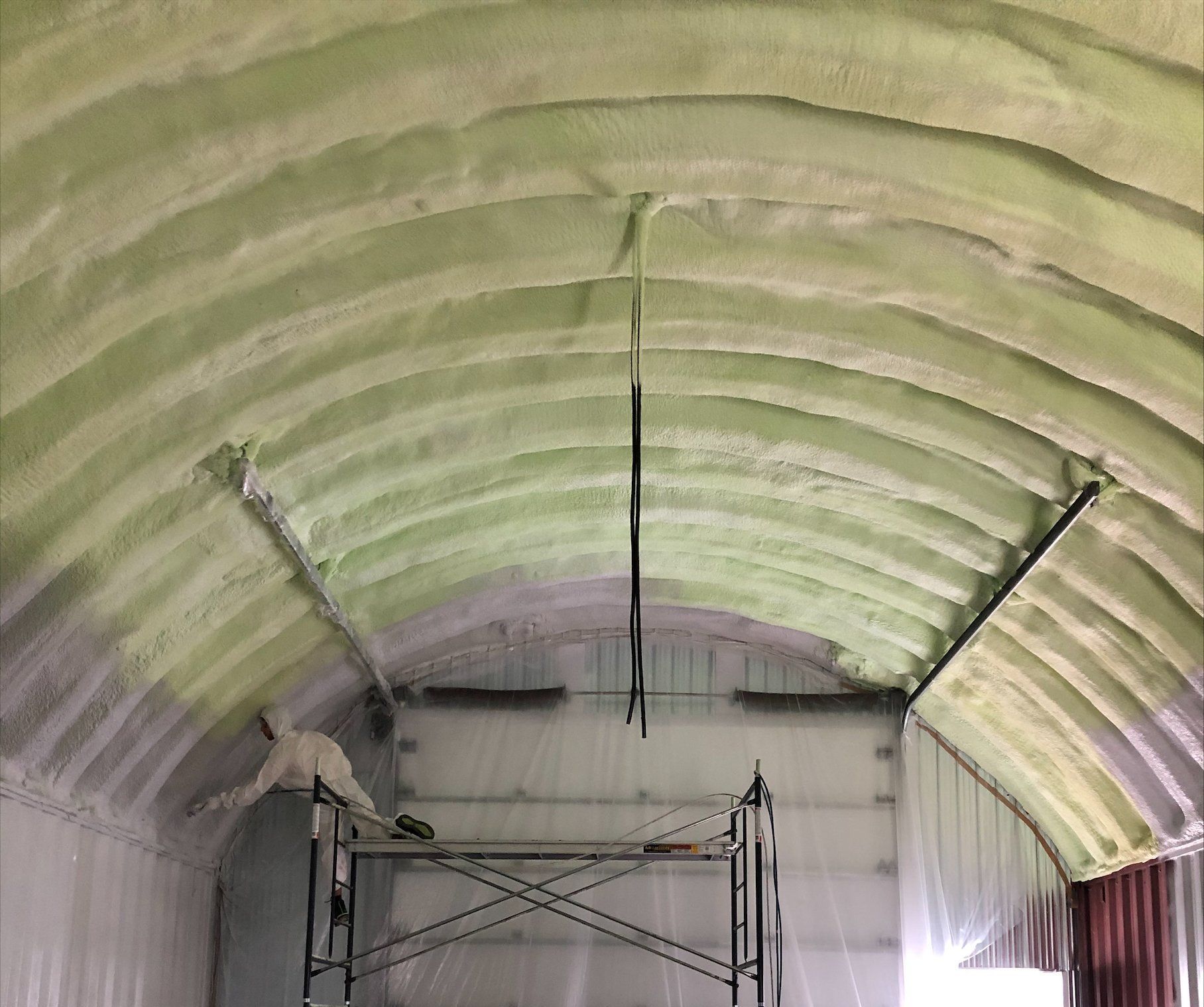 Vue intérieure d'un plafond voûté recouvert d'isolant vert. Un échafaudage est positionné en dessous.