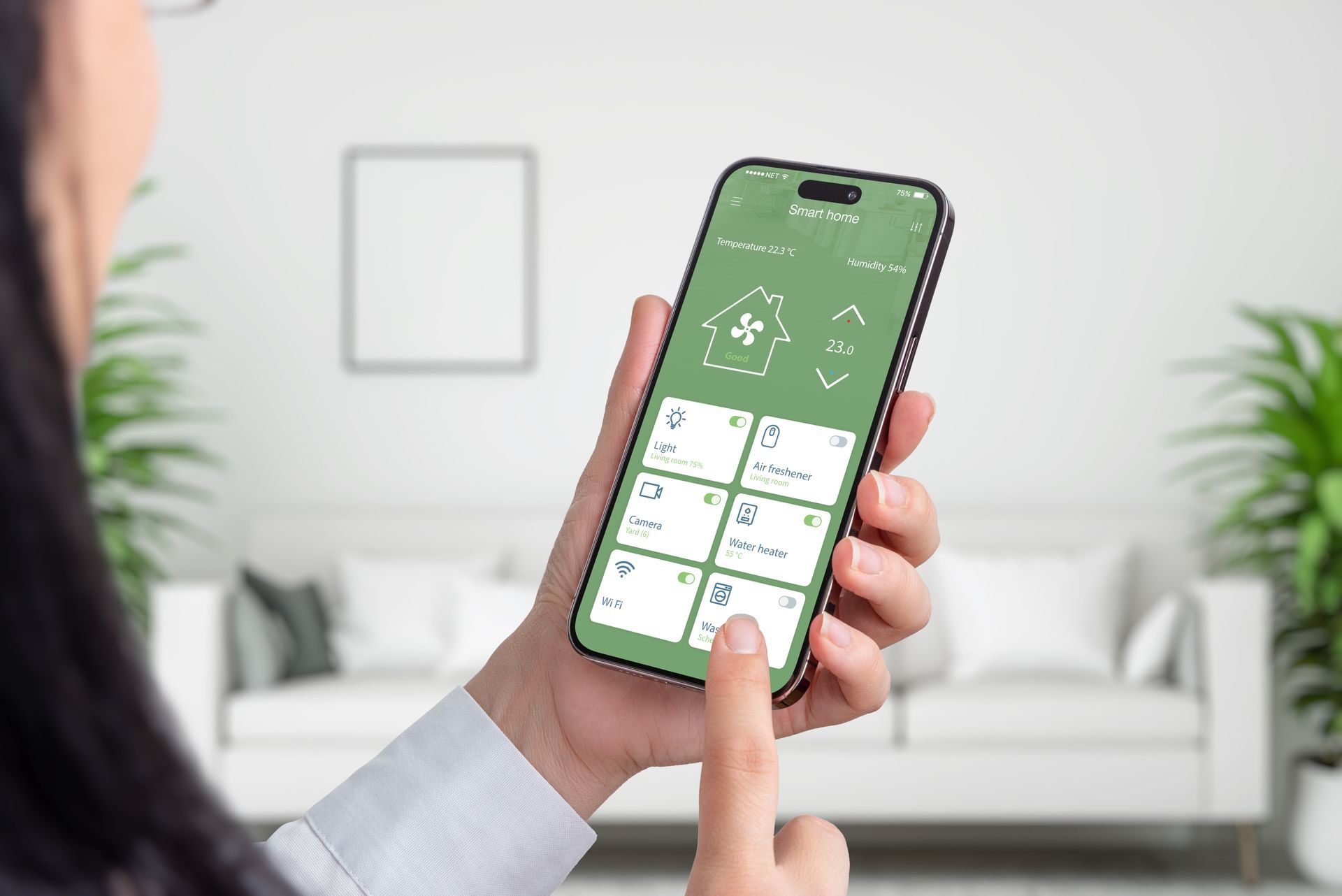 Person holding a smartphone with a green smart home control app on screen in a living room