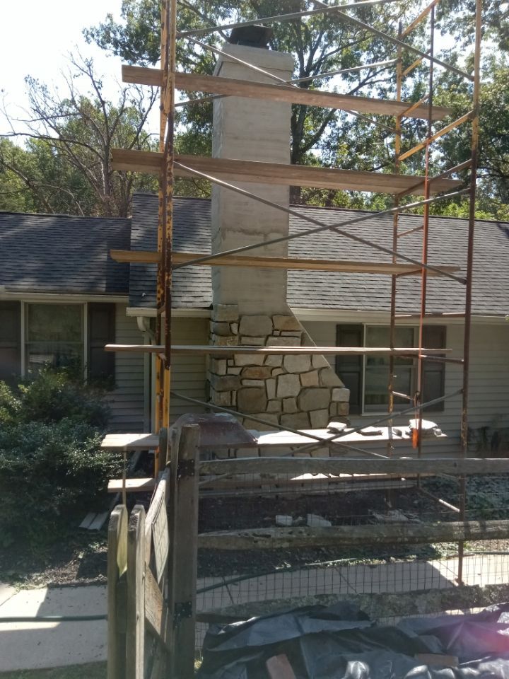 Brick chimney under construction with scaffolding in front of a house