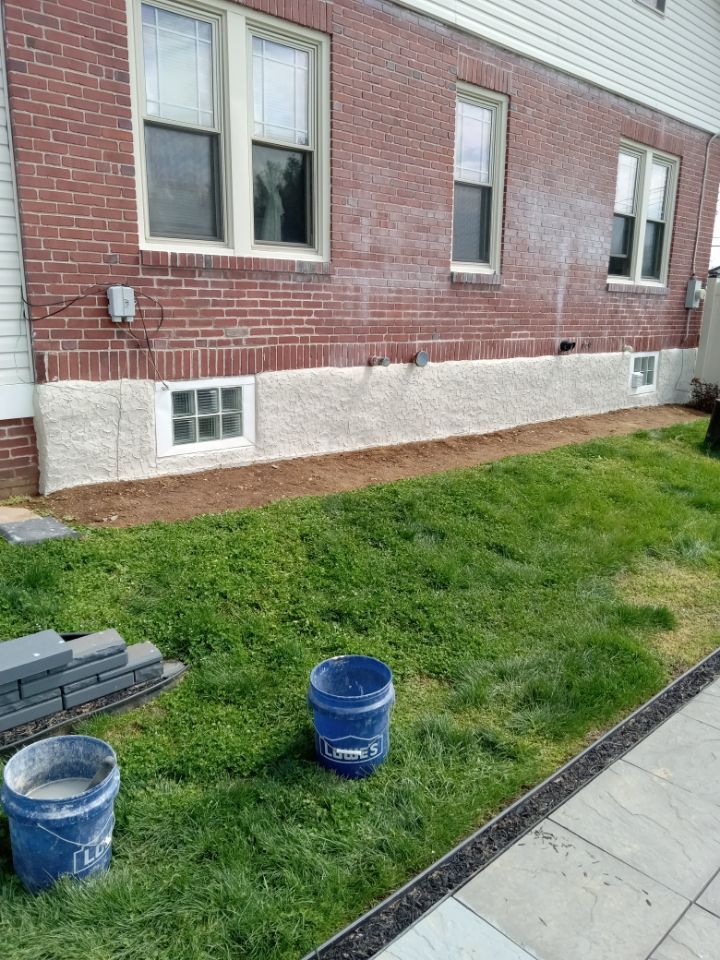 Brick building wall with windows, grassy strip, sidewalk, and two blue buckets in the foreground.
