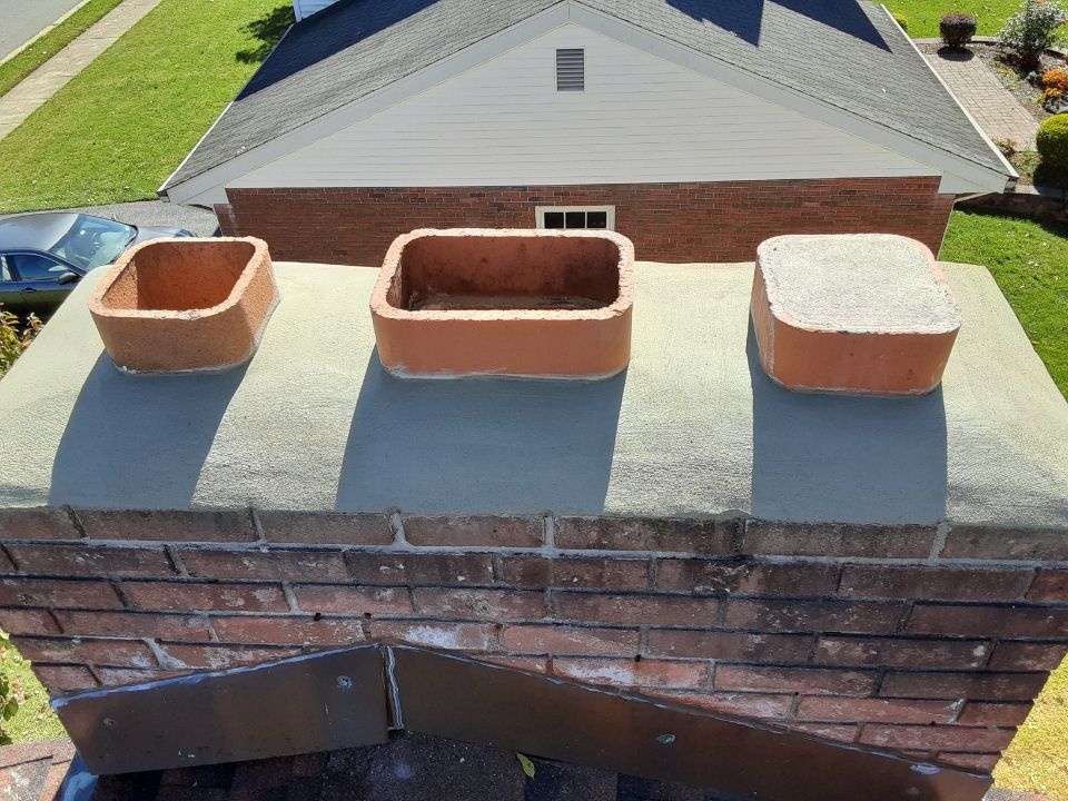 Three terracotta planters on a flat brick chimney cap, with a house roof and lawn in the background