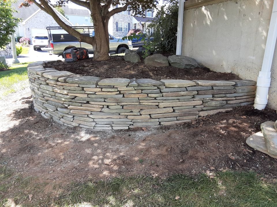 Stone retaining wall around a tree in a front yard, with a car and house in the background.