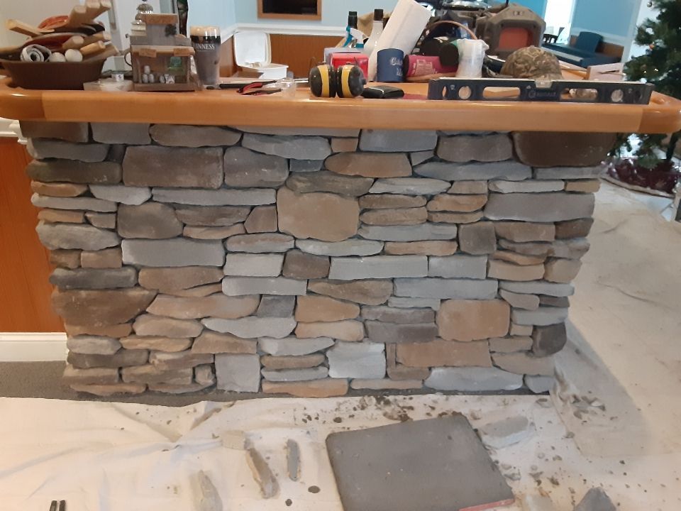 Stone-faced kitchen island under renovation with tools and mortar on the floor