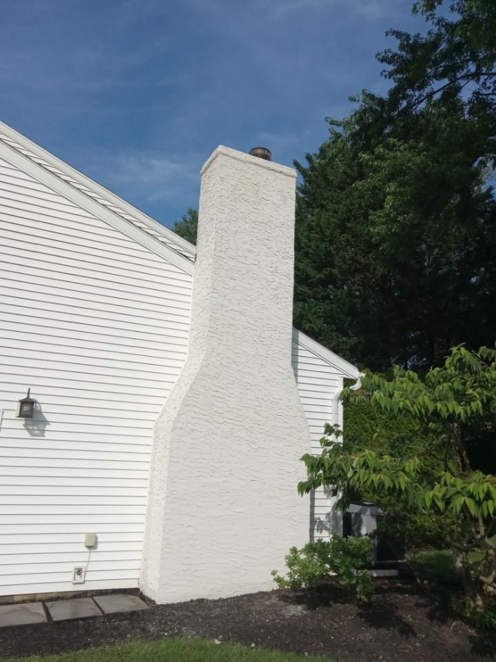 White house exterior with a tall brick chimney beside a leafy garden under a blue sky