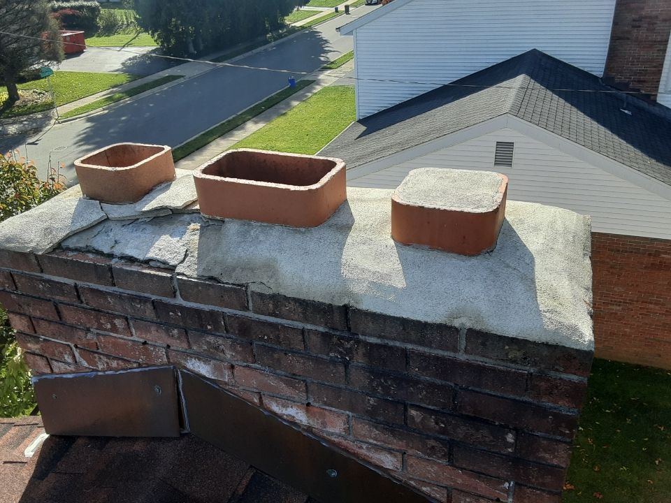Brick chimney with three red clay flue caps on a rooftop, viewed from above