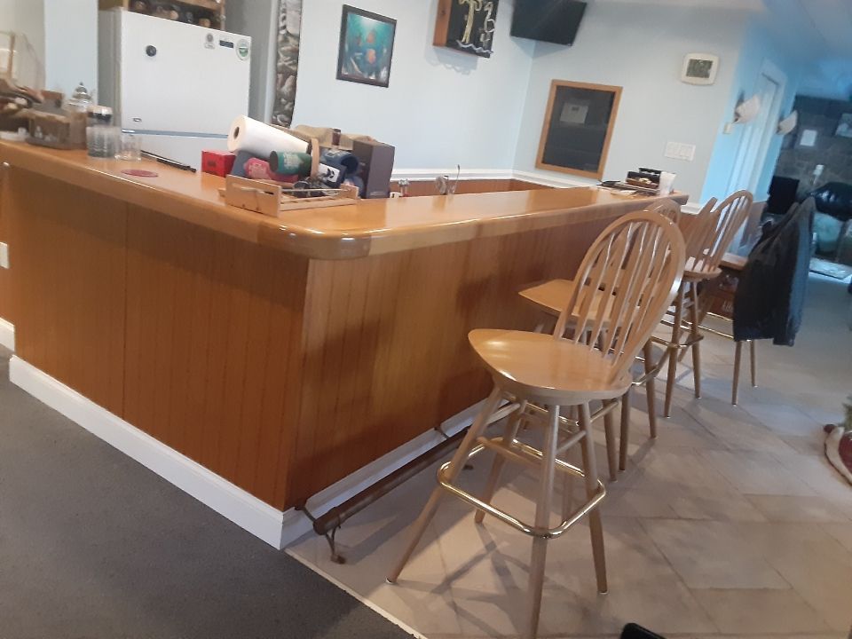 Wooden kitchen bar with stools in a tiled home interior, with a bright entryway in the background