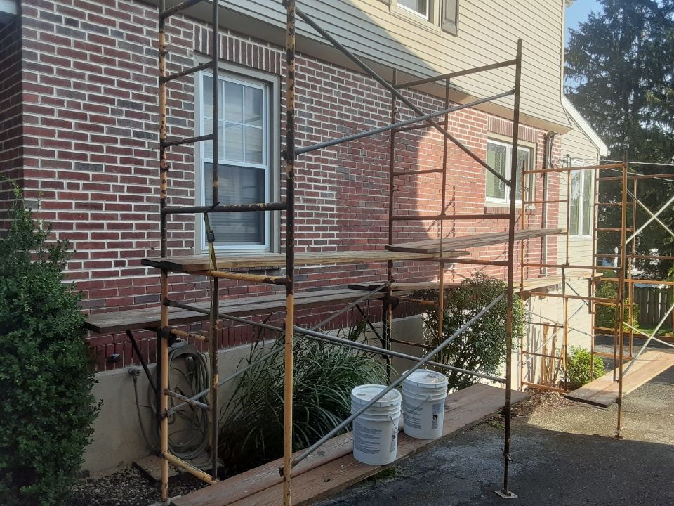 Scaffolding beside a brick house, with buckets and a window under repair on a sunny day