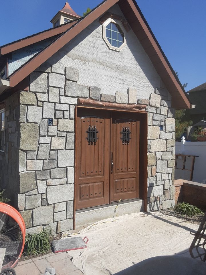 Small stone building with wooden double doors and an octagonal window under a steep roof.