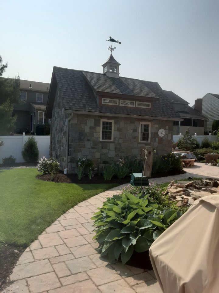 Small stone garden shed with flower beds and a stone path in a backyard