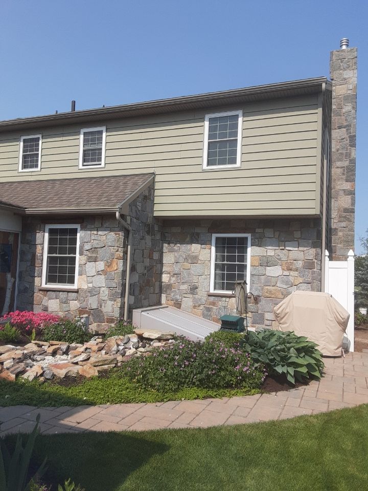 Two-story house with stone and beige siding, front garden, walkway, and a covered grill in the yard