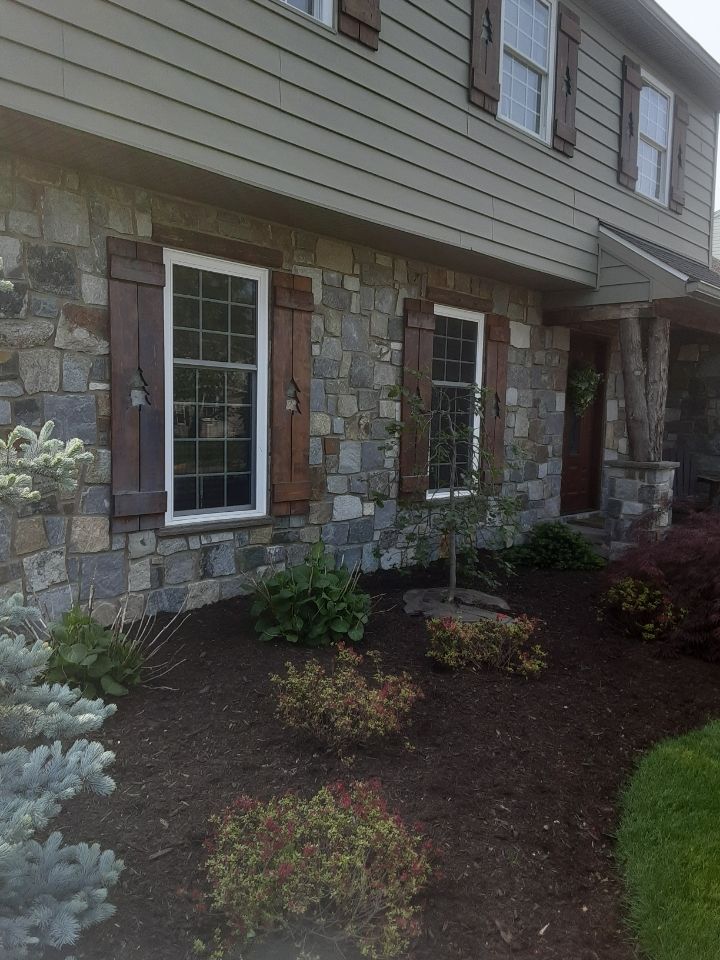 Stone-front house exterior with windows and small landscaped shrubs along the foundation