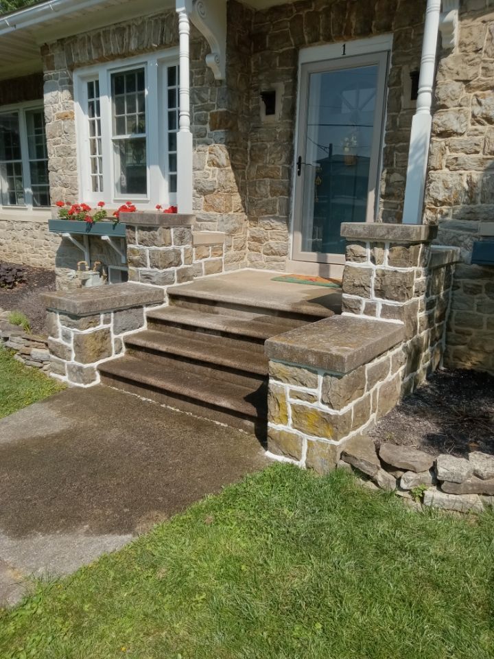 Stone house front porch with steps, blue door, and flower boxes beside a lawn