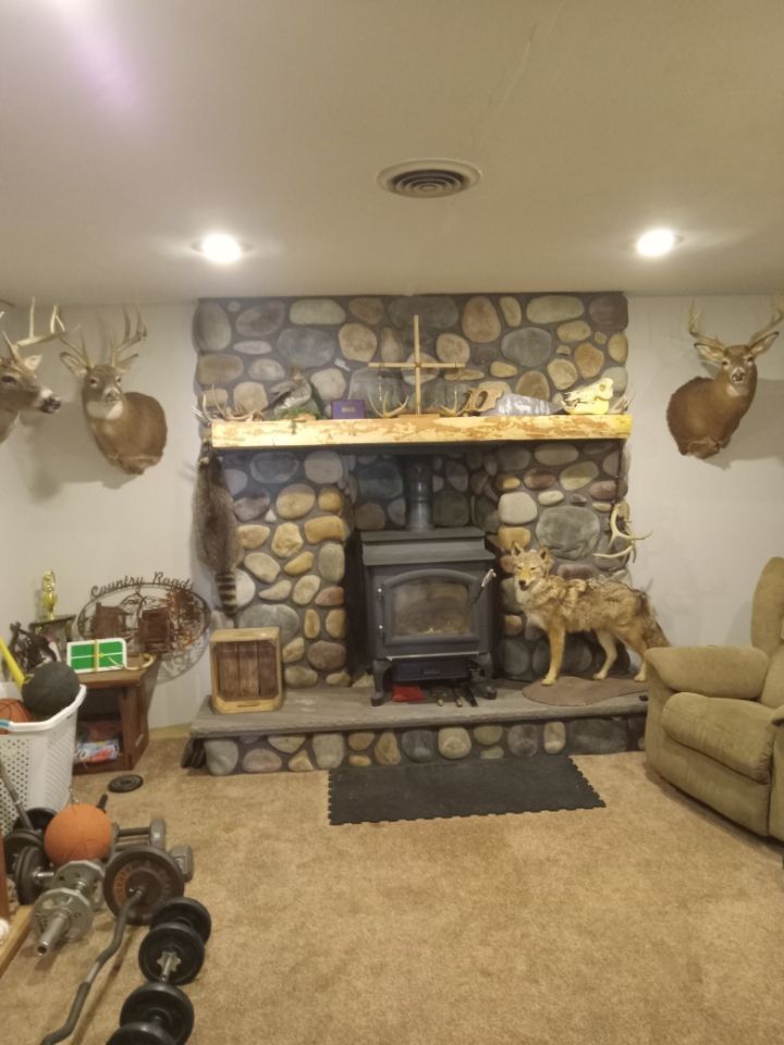 Cozy living room with stone fireplace, mounted deer heads, beige couch, and exercise weights in the foreground
