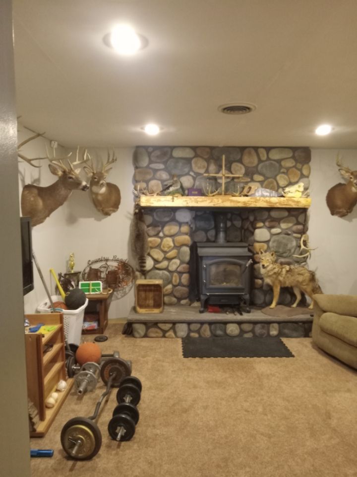 Cozy living room with stone fireplace, mounted deer heads, beige sofa, and dumbbells on the floor