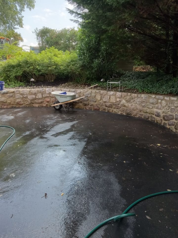 Wet backyard patio with a stone wall, wheelbarrow, and green hose after rain