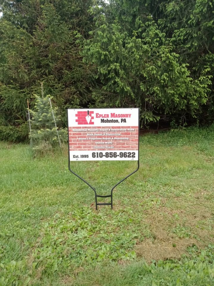 Sign for a masonry business on a metal stand in a grassy yard, with trees in the background.