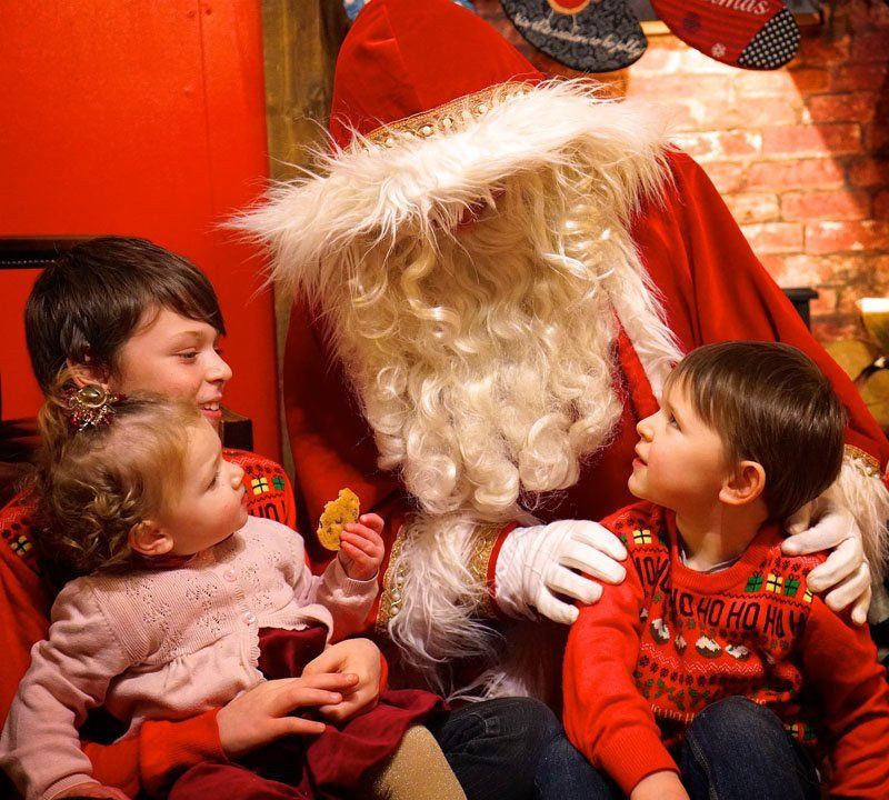 Santa Claus with three children, one holds a cookie. Festive red background.
