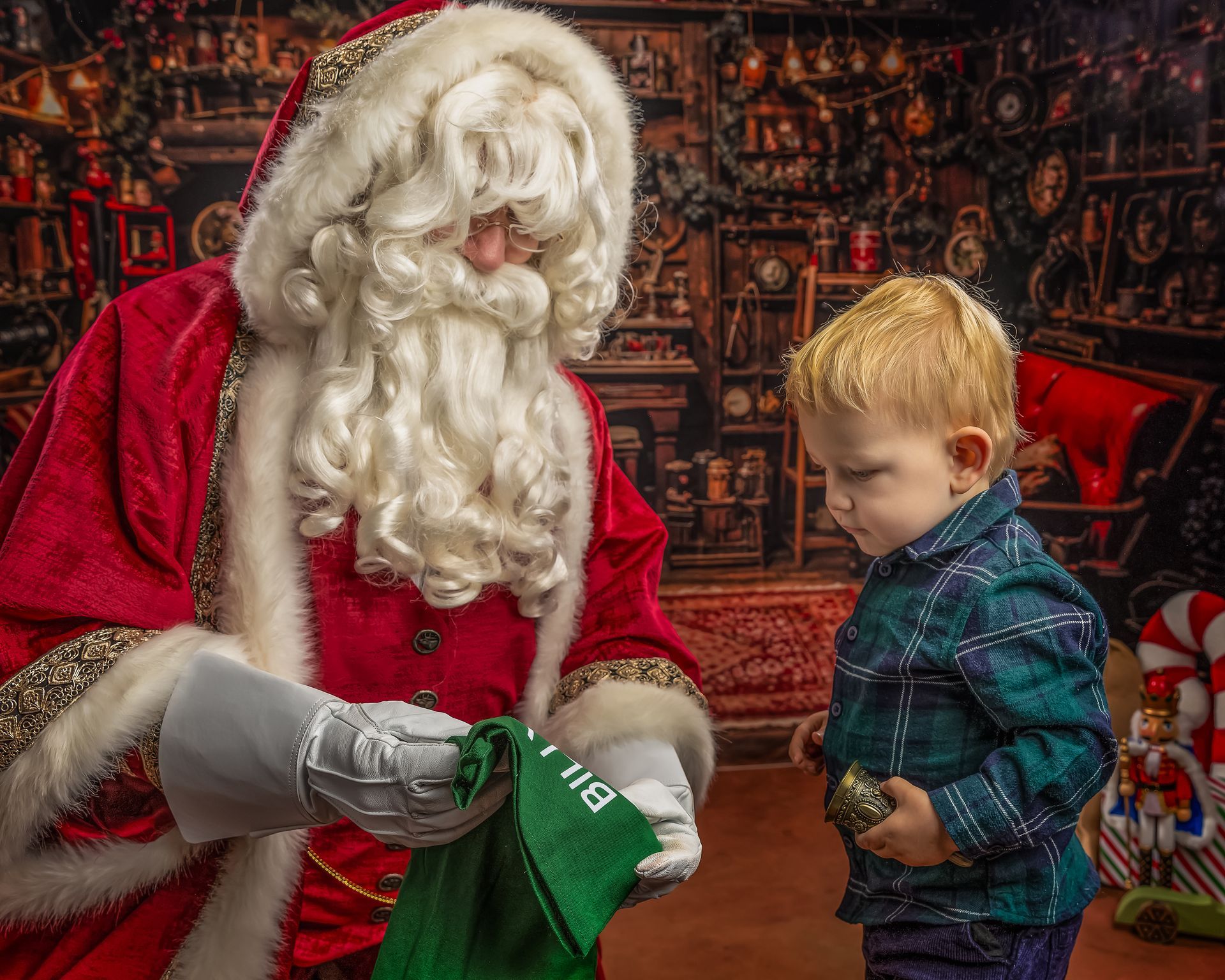 Boy hugging Santa Claus, red suit, white beard, Christmas tree in background.